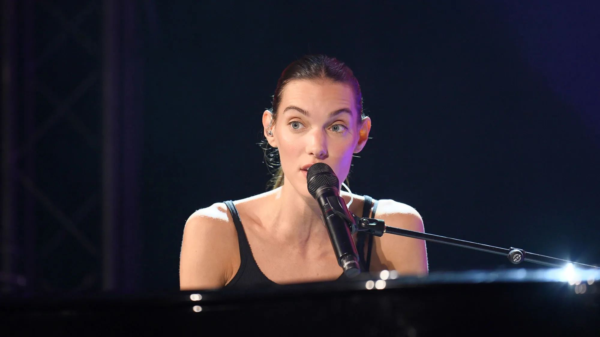 Une chanteuse au micro derrière son piano, en gros plan sur une scène sombre