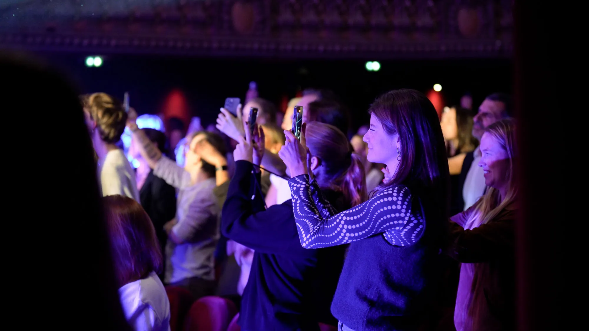 Des spectatrices filment un concert au téléphone dans une salle éclairée de violet