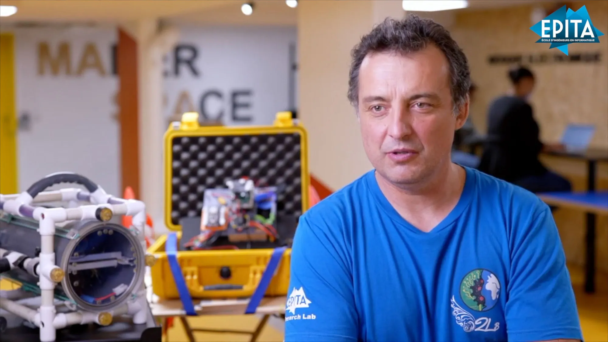 Un chercheur en interview devant un prototype de robot sous-marin dans un atelier universitaire
