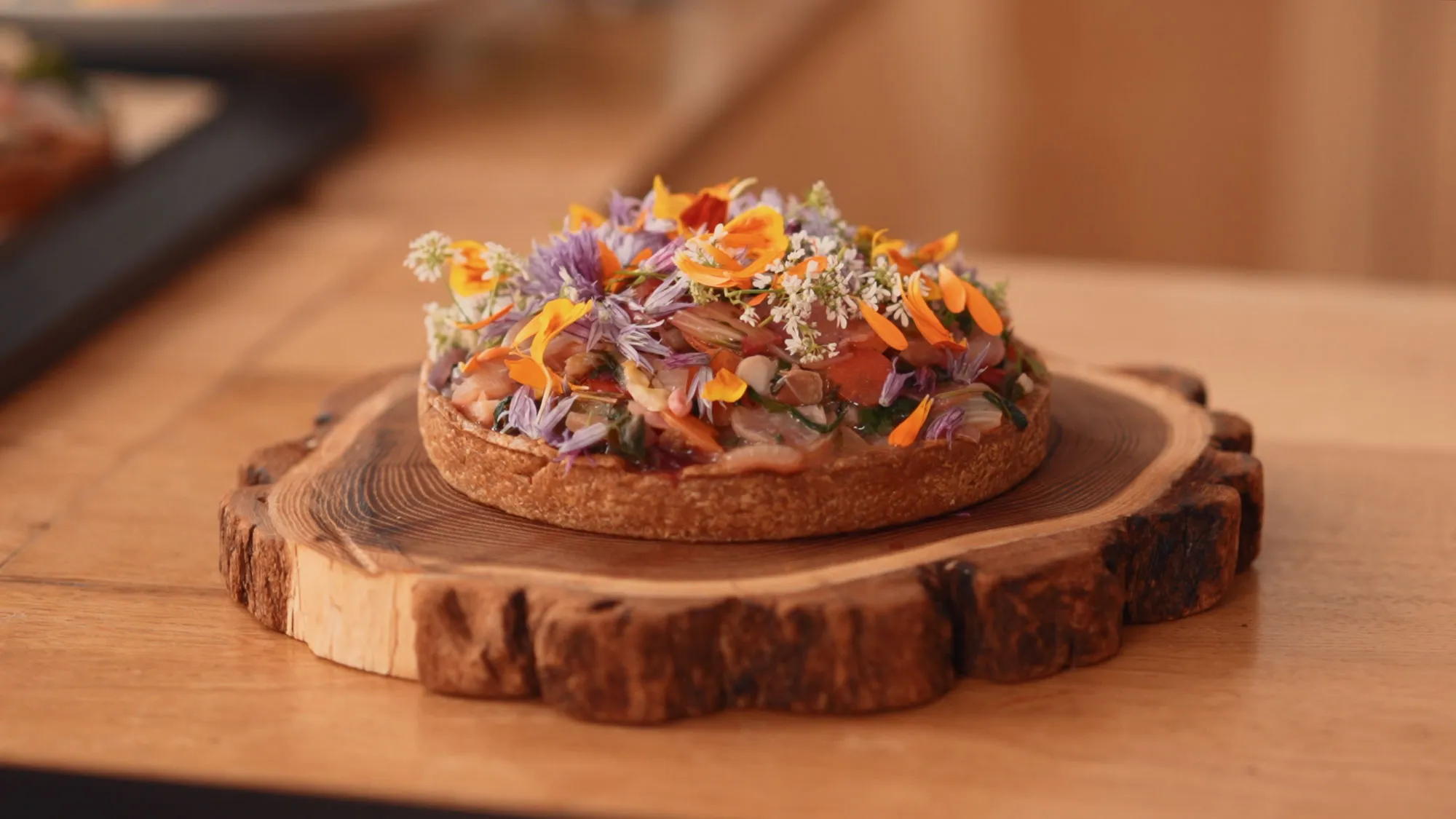 Une tarte garnie de fleurs comestibles posée sur un plateau de bois