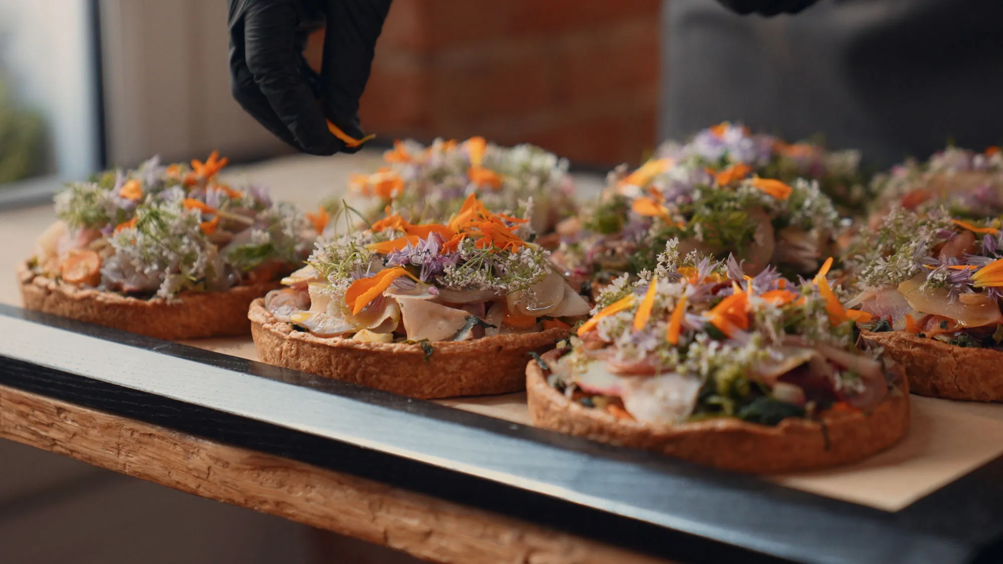 Un cuisinier ganté dresse des tartes garnies de fleurs comestibles sur une planche