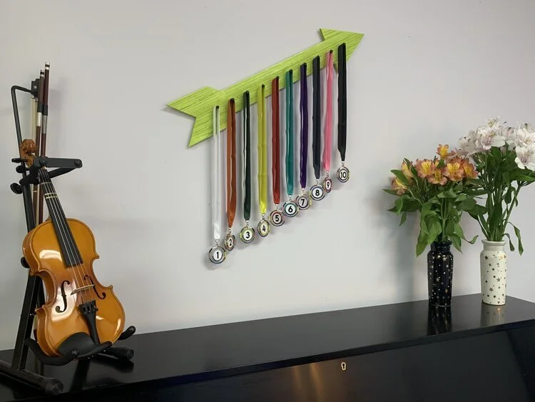 Violin displayed on a wall with colorful award ribbons