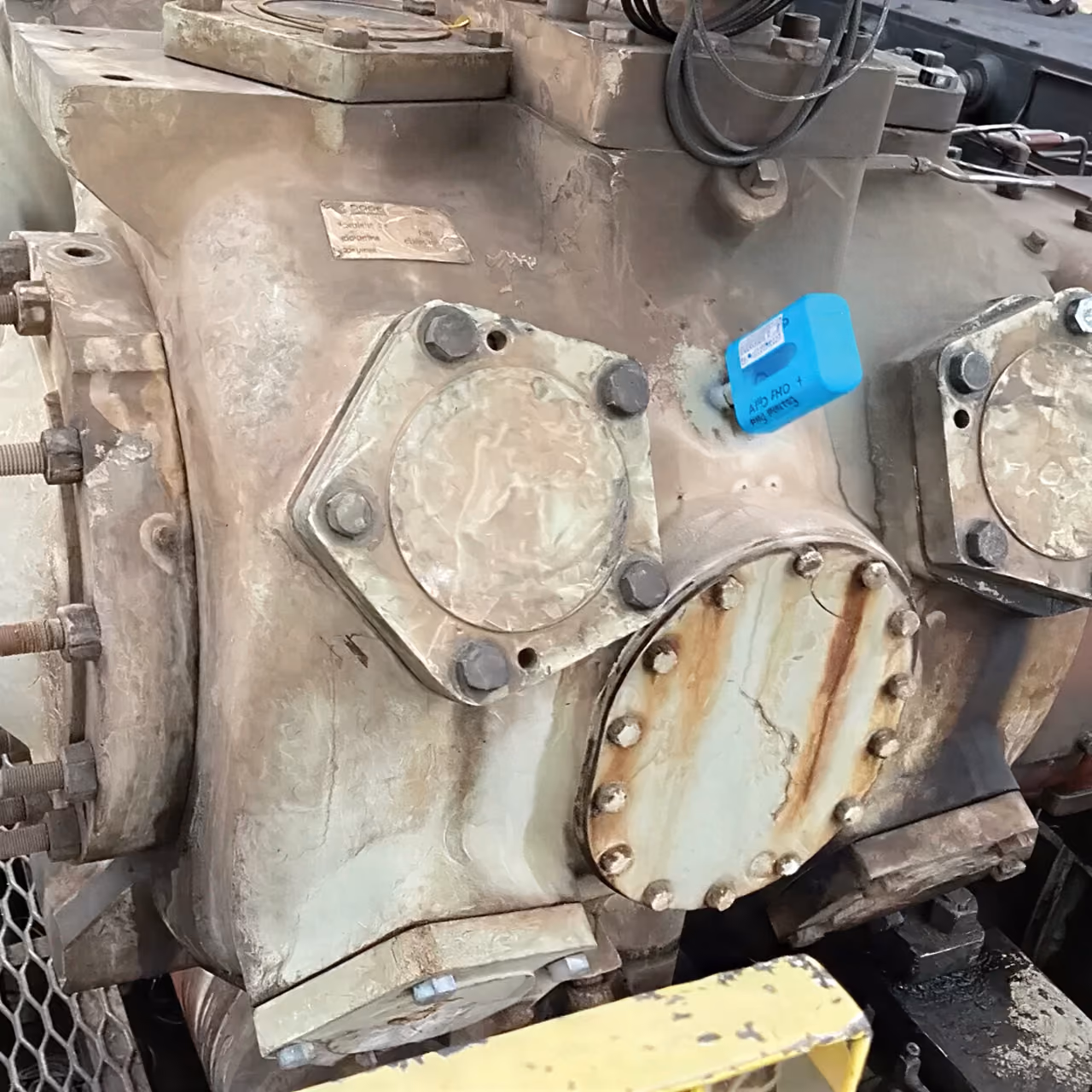 Close-up of a weathered industrial machine with rusted bolts and a blue sensor attached.