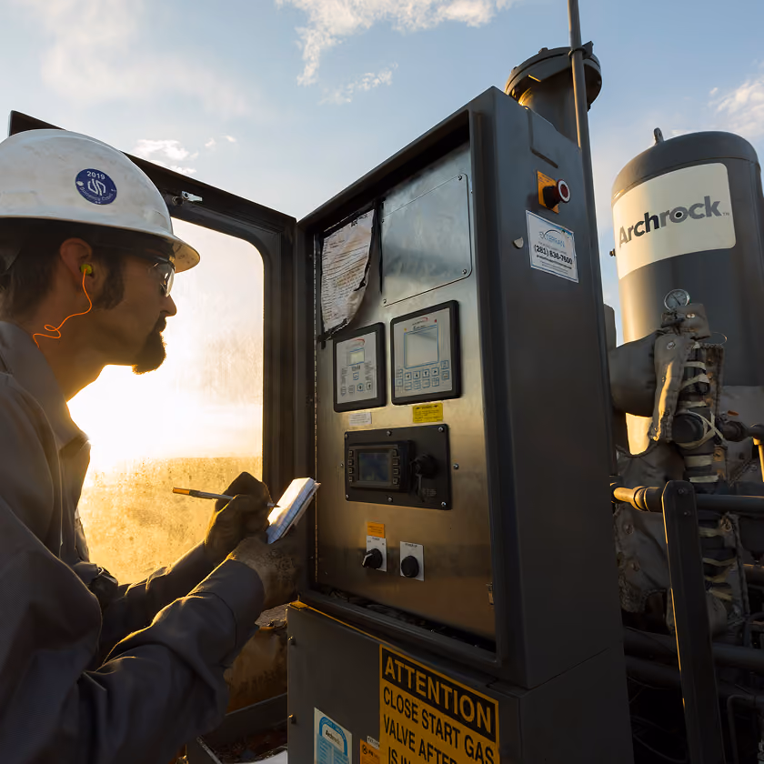 Worker in safety gear checks an industrial control panel at sunset near equipment labeled Archrock.