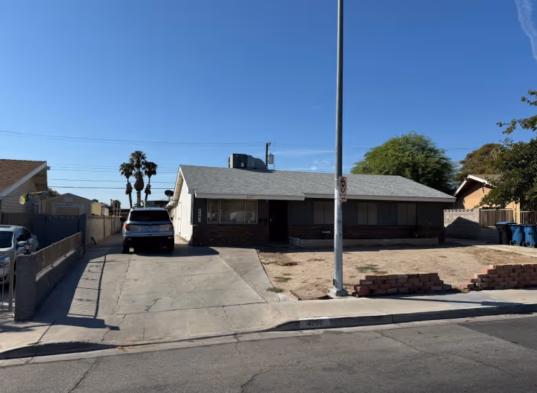 Single-story house with a large driveway and dry front yard under a clear blue sky.