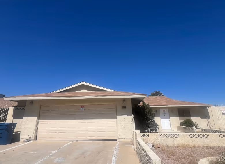 Single-story house with a closed beige garage door, a white front door, and a clear blue sky overhead.