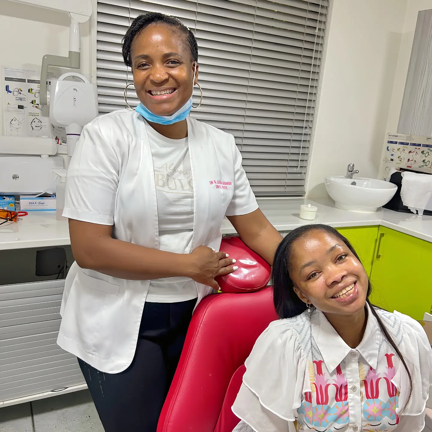 Smiling dentist in white coat stands beside a happy female patient in a dental clinic chair at Dr Lehong Shabangu Dental.