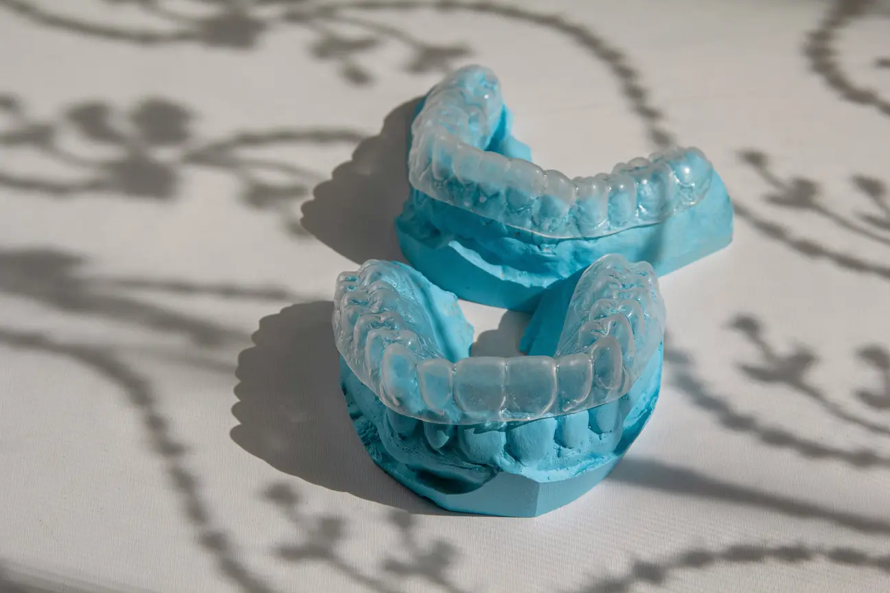 Clear dental aligners placed on blue dental molds casting shadows on white surface.