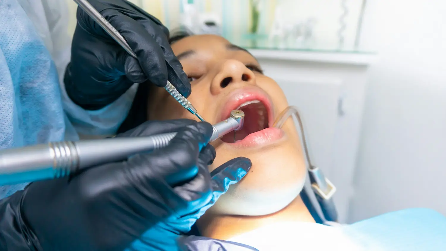Close-up of a woman receiving a dental cleaning with instruments in a clinic setting.