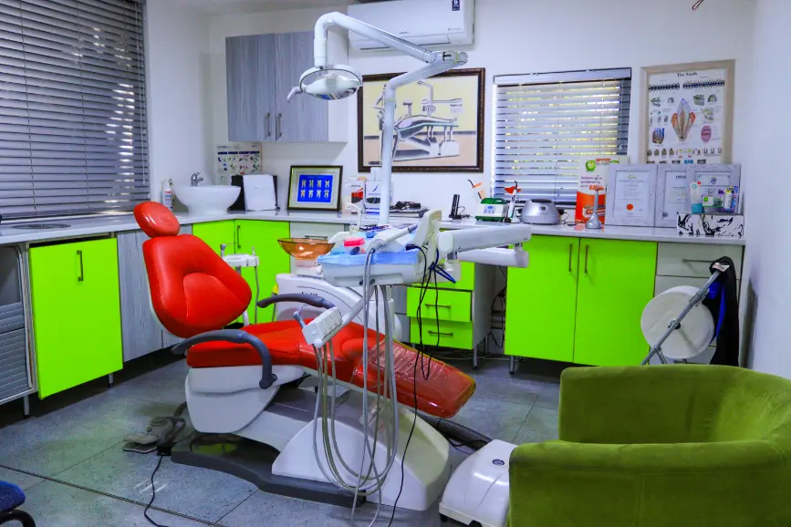 Modern dental clinic interior with red dental chair, green cabinets, and dental equipment.