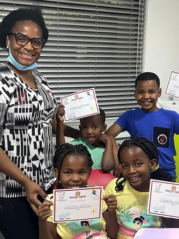 Smiling woman and four children holding bravery awards in a brightly lit room with blinds.
