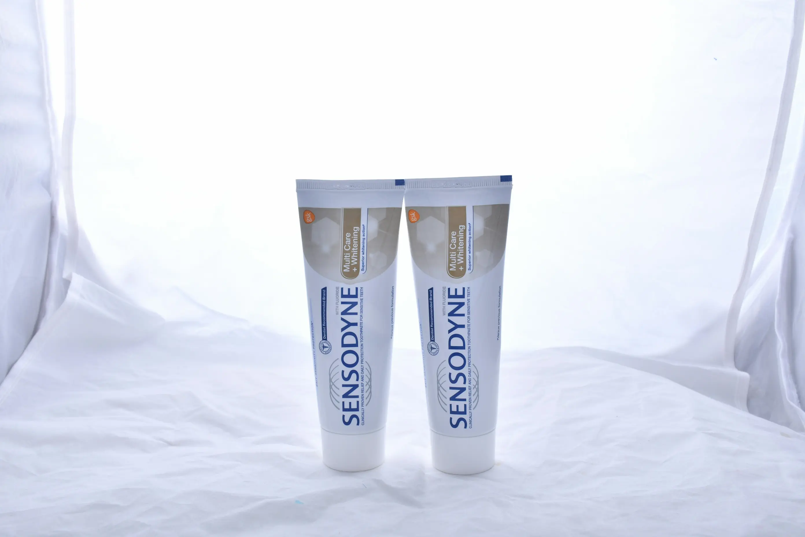 Two tubes of Sensodyne Multi Care + Whitening toothpaste standing on a white fabric surface.