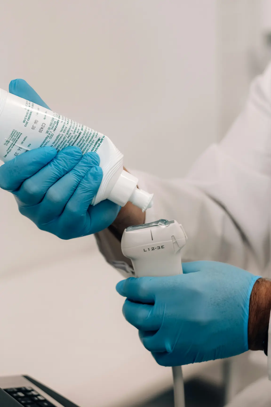 Person with blue gloves applying gel to ultrasound transducer probe.