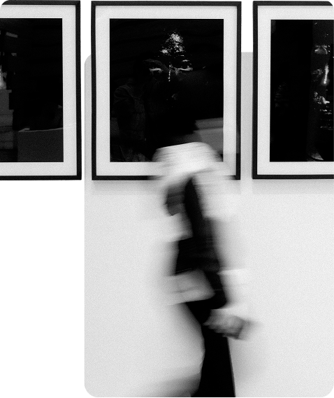 Figure in a long dress walking past framed prints in a gallery