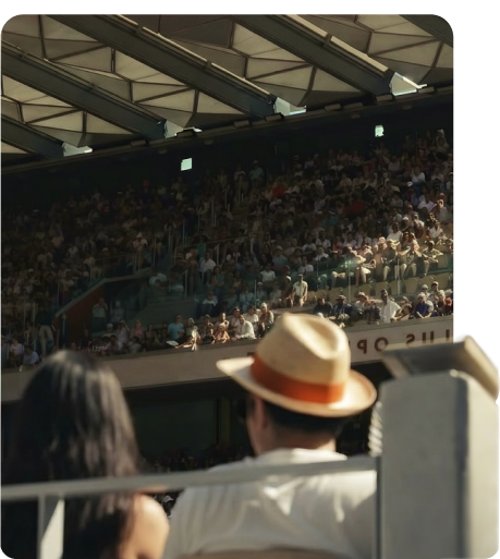Spectators in a stadium stand, one in a straw panama hat