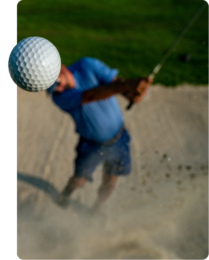 Golfer playing out of a sand bunker as the ball flies toward the camera