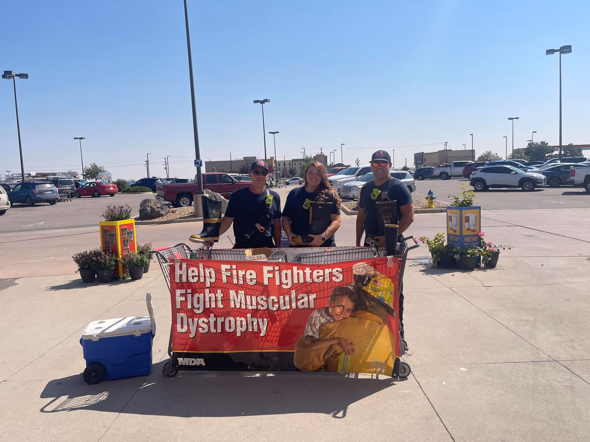 Three firefighters stand behind a cart with a banner to help fight muscular dystrophy.