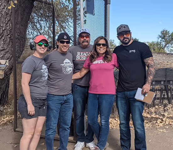 Five people standing outdoors posing with casual clothes and sunglasses on a sunny day.