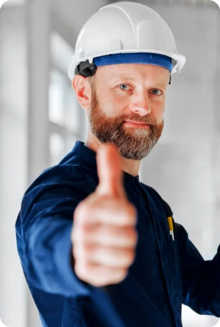 Bearded construction worker in blue uniform and white helmet giving a thumbs-up.
