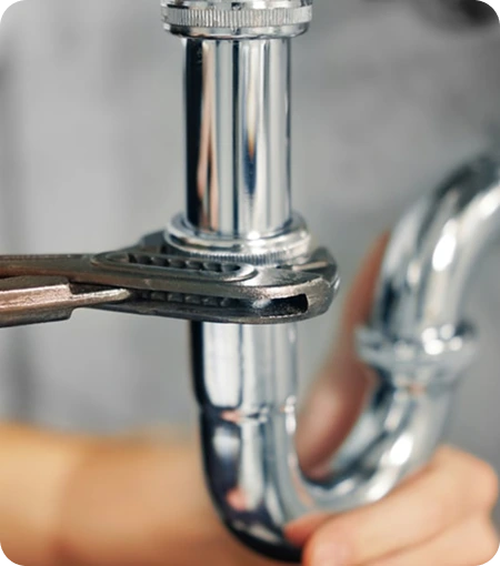 Hand holding a pipe wrench tightening a shiny chrome plumbing pipe joint.