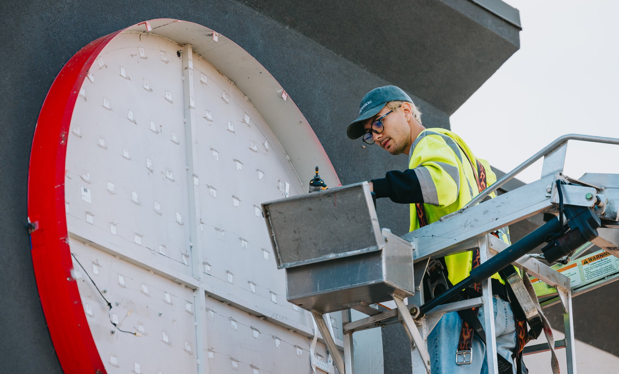 Rick Signs technician in bucket truck repairing an exterior wall-pack light at a Chicago commercial property