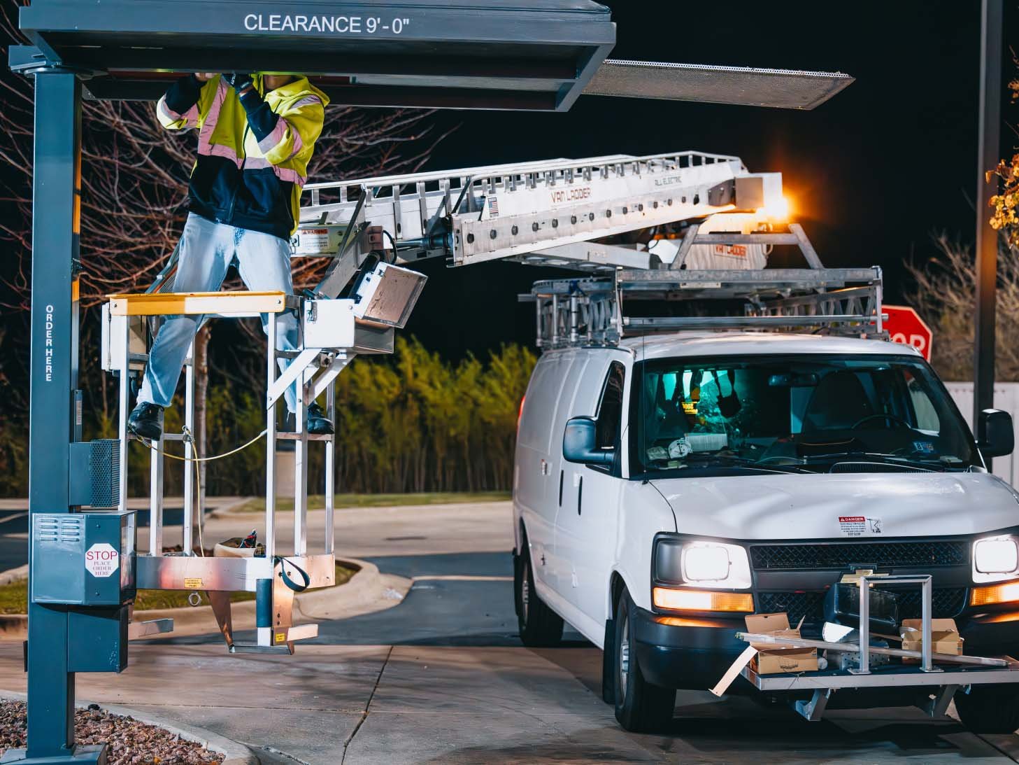 Rick Signs bucket truck and service van on a night emergency sign repair call beneath an overhead clearance pole in Chicago
