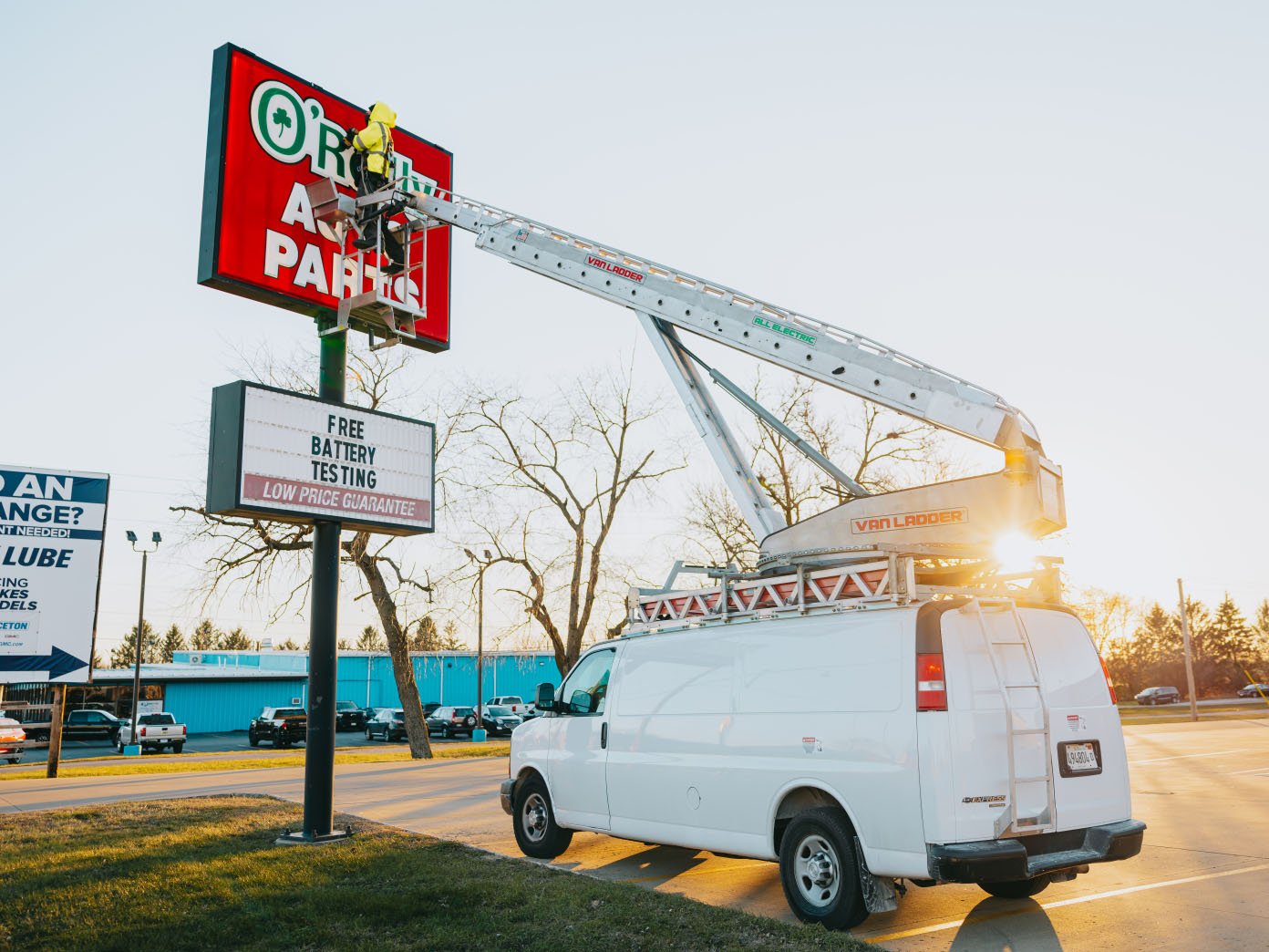 Rick Signs Van Ladder bucket truck and service van at sunset beside a tall pole sign during a storm-cleanup repair in Chicago