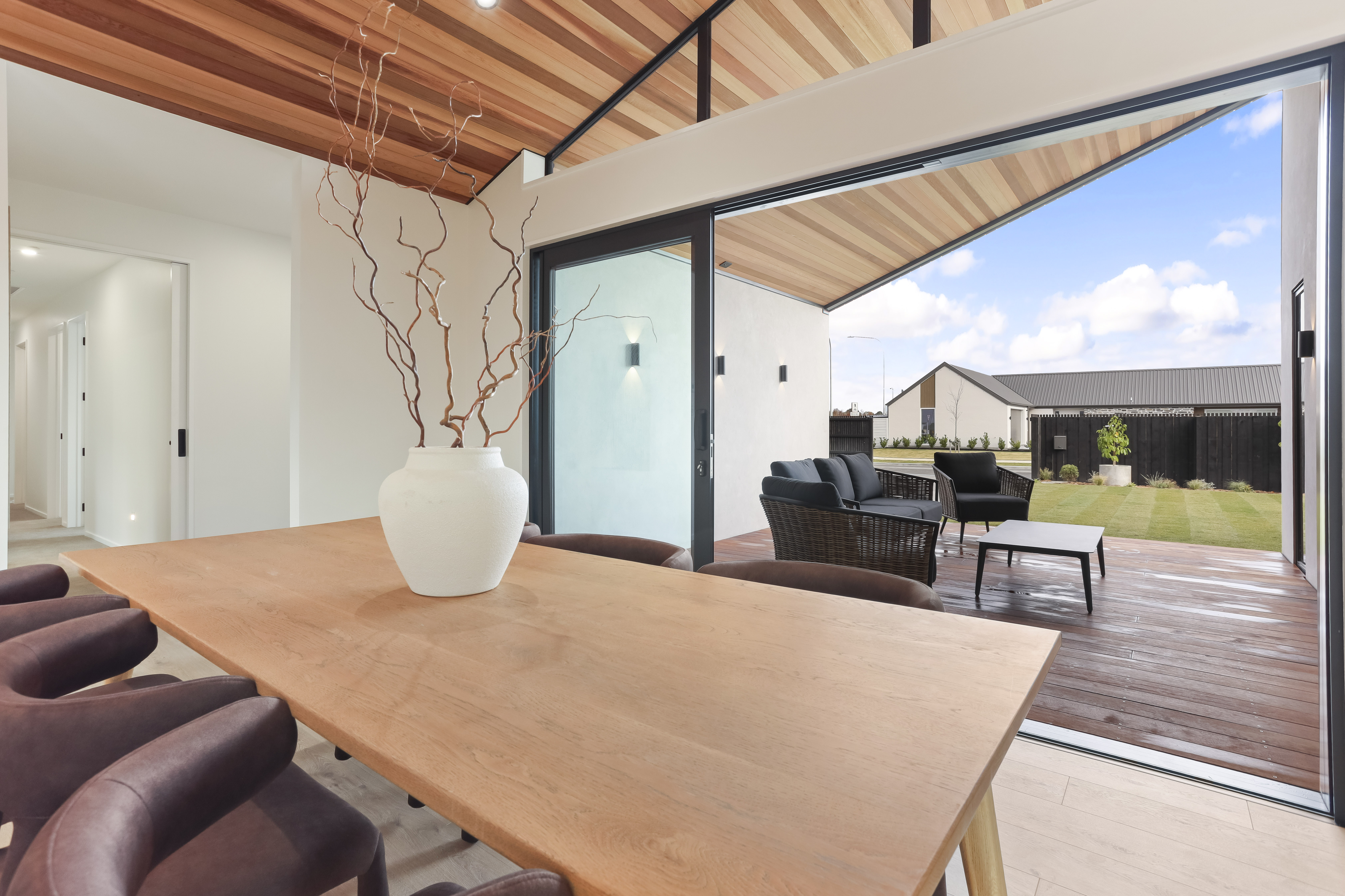 Modern dining area with wooden table and chairs next to large sliding doors opening to patio with seating.