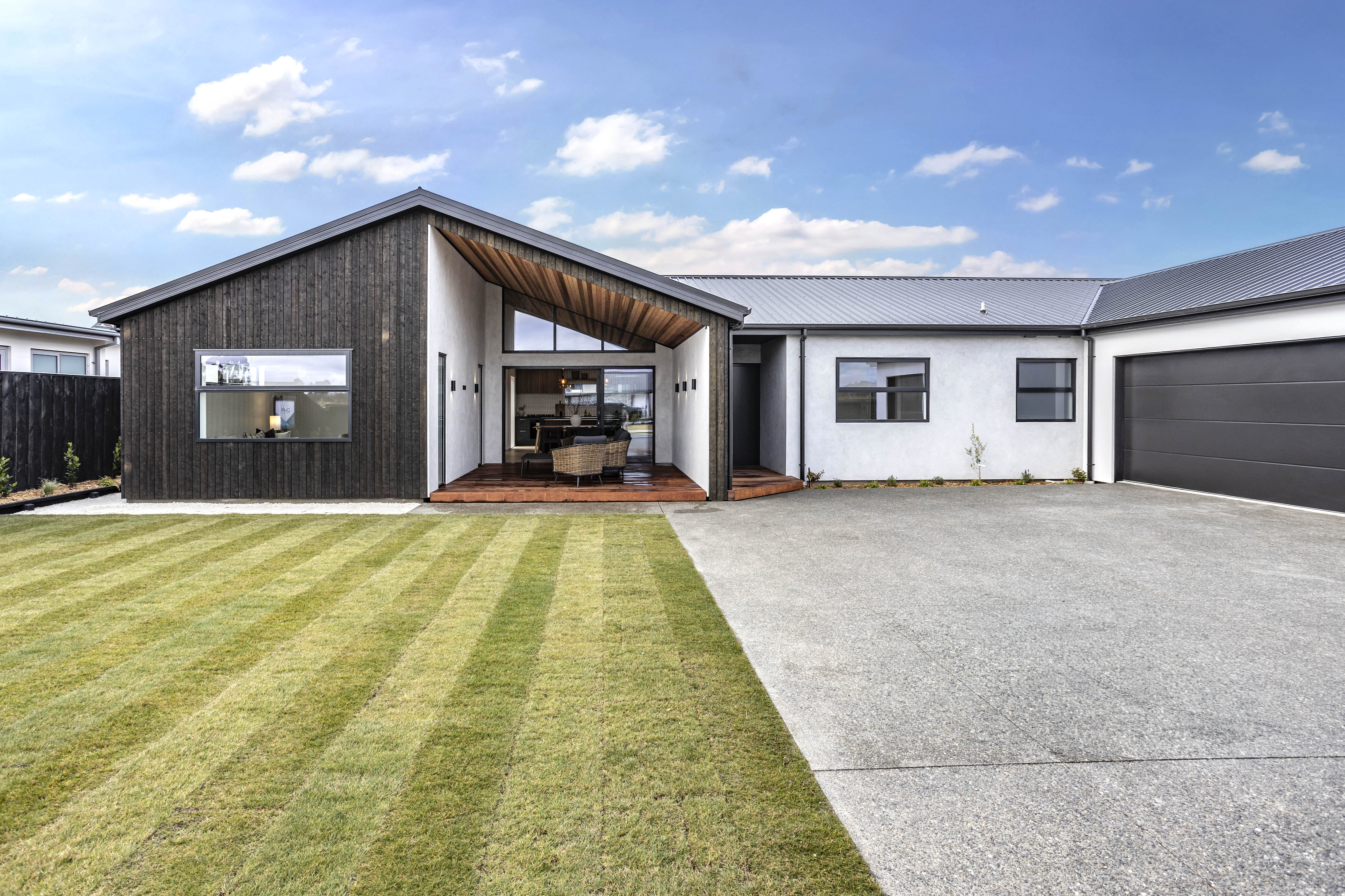 Modern house with dark wood siding, white walls, triangular porch, lawn, and large driveway.