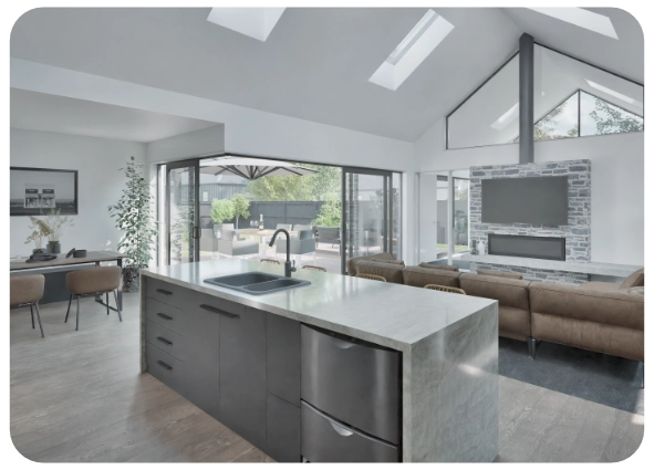 Modern open-plan kitchen and living room with island, brown couch, and outdoor patio visible through glass doors.