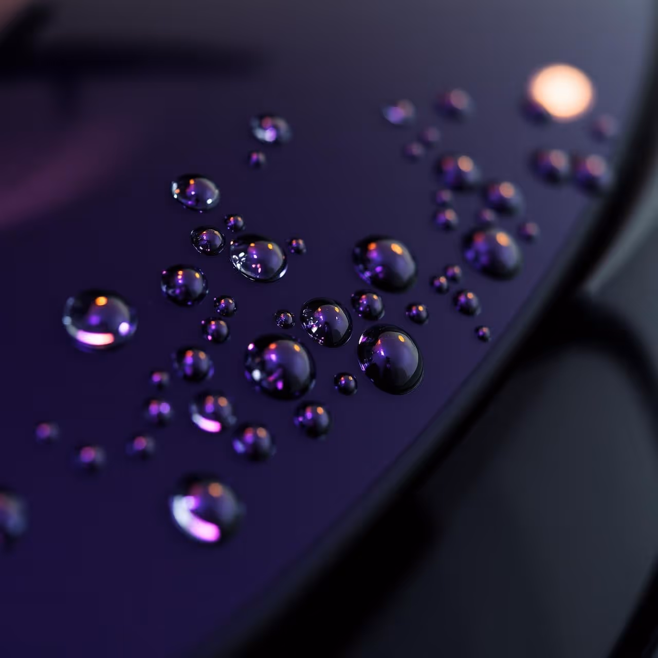 Close-up of water droplets on a smooth dark purple surface with light reflections.