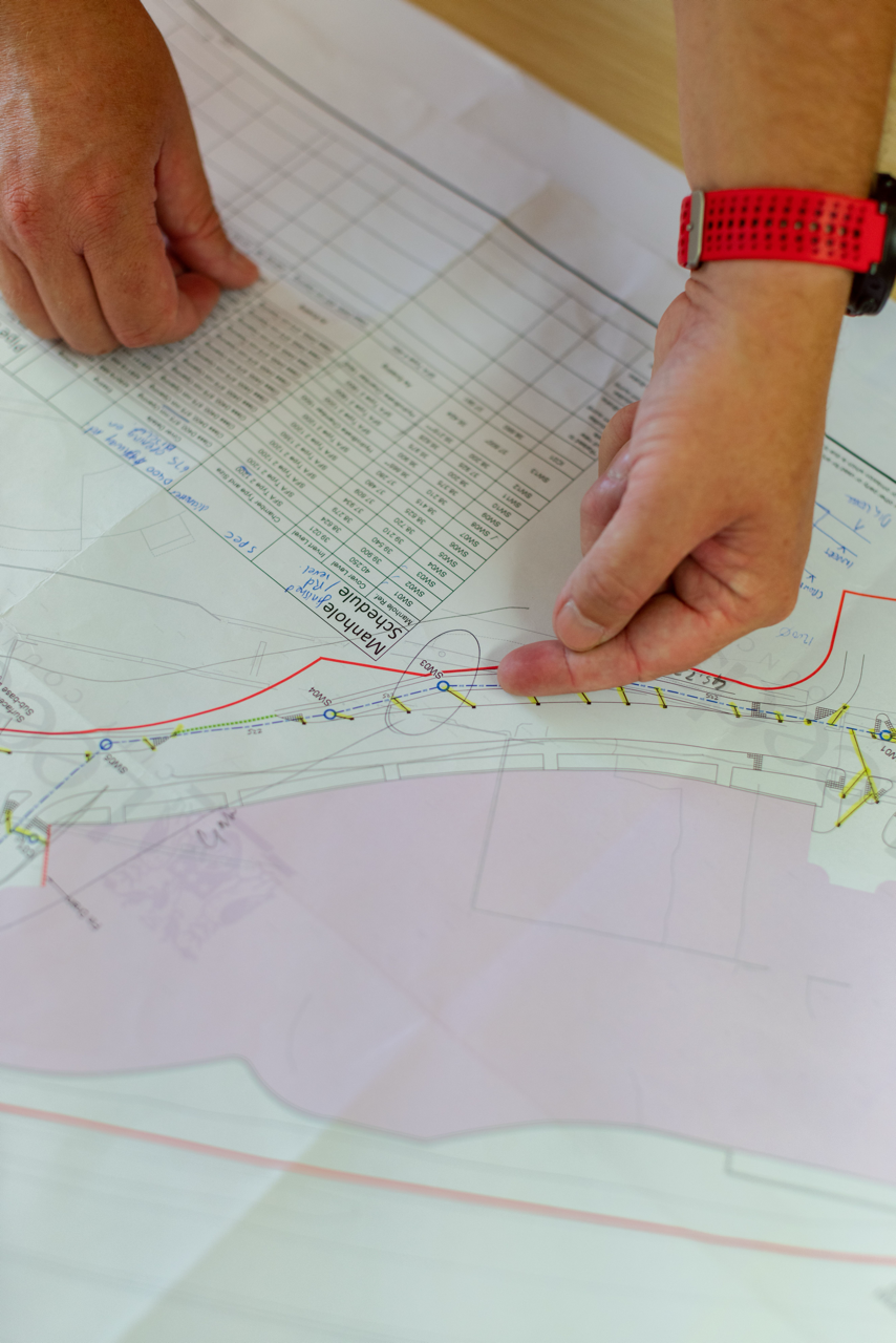 Hands pointing and touching a detailed architectural or engineering plan on paper with tables and diagrams.