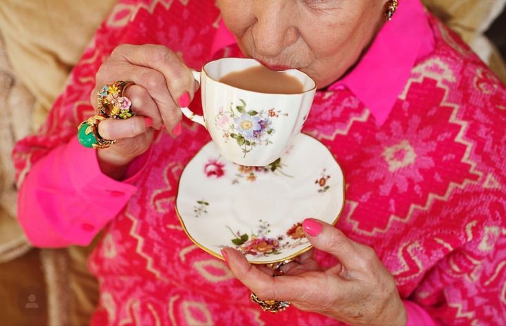 An older woman in a pink jumper enjoying a cup of tea