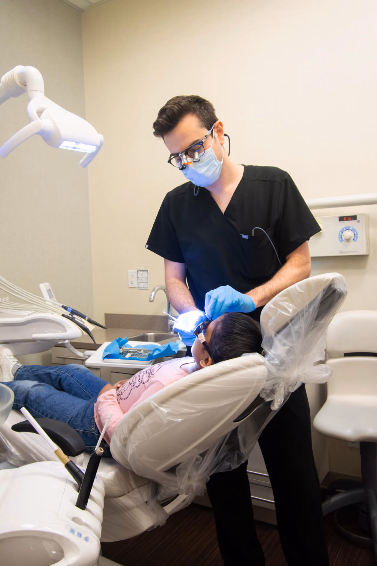 Dentist in black scrubs and mask treating a child patient lying back in a dental chair.
