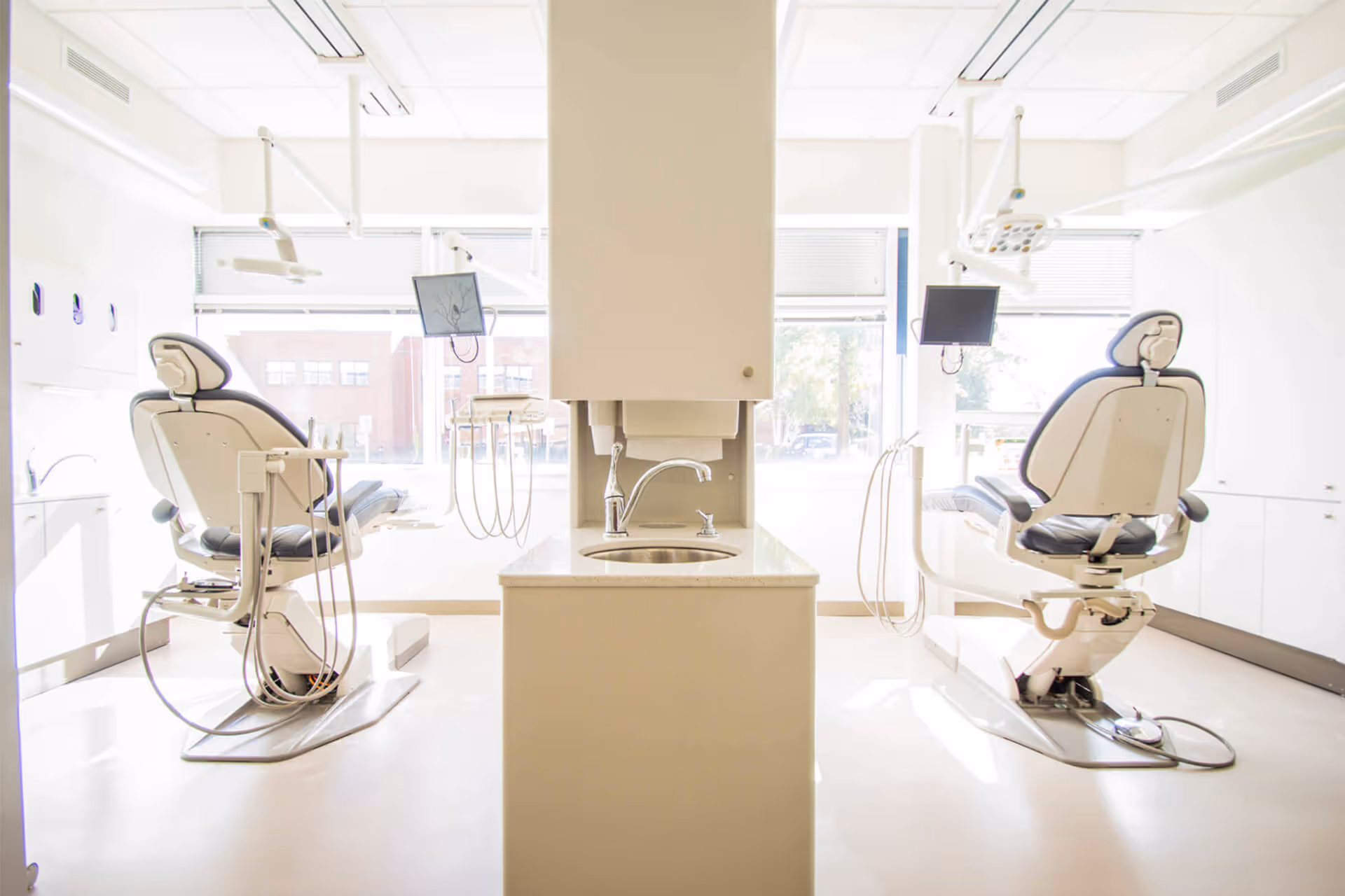 Bright dental office room with two modern dental chairs and equipment on either side of a central sink.