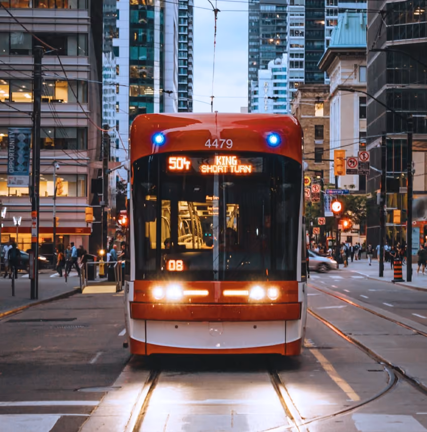 Front view of a red and white streetcar on city tracks with buildings and pedestrians in the background.