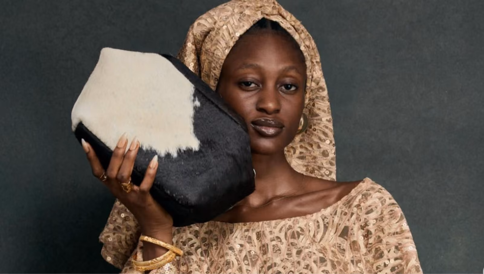 Woman in beige patterned outfit and headscarf holds a black and white Claic Designs fur clutch near her face.