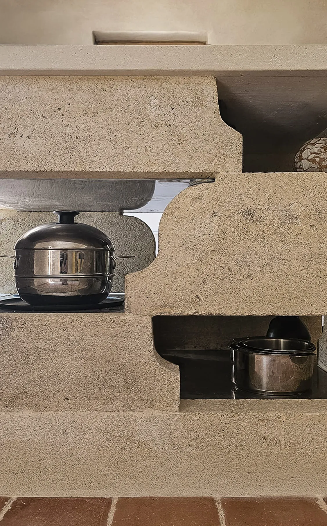 Two stainless steel pots stored in custom beige stone kitchen shelves with curved cutouts.