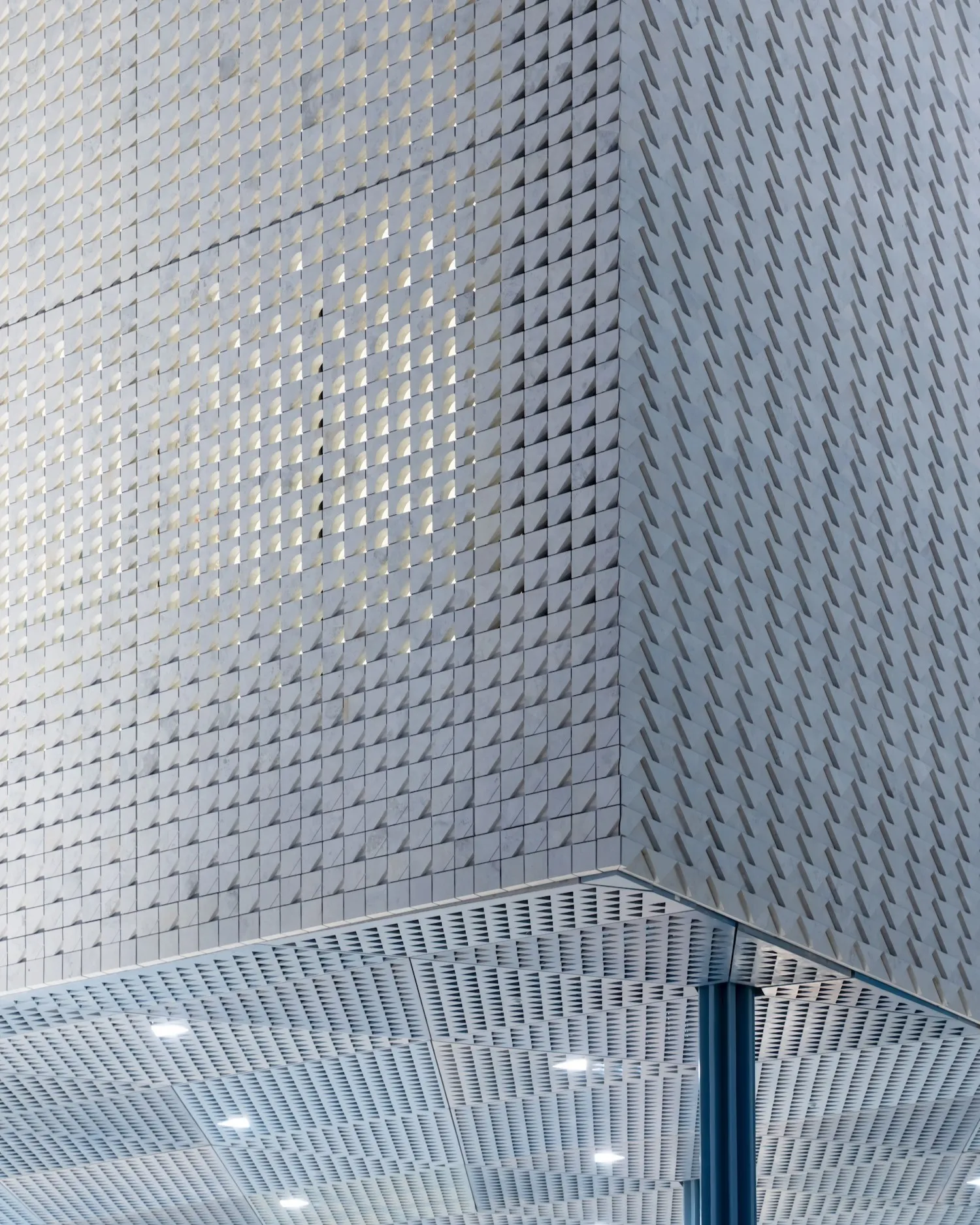 Houston Ismaili Center - Close-up of building corner with textured stone tile facade and perforated ceiling with lights.