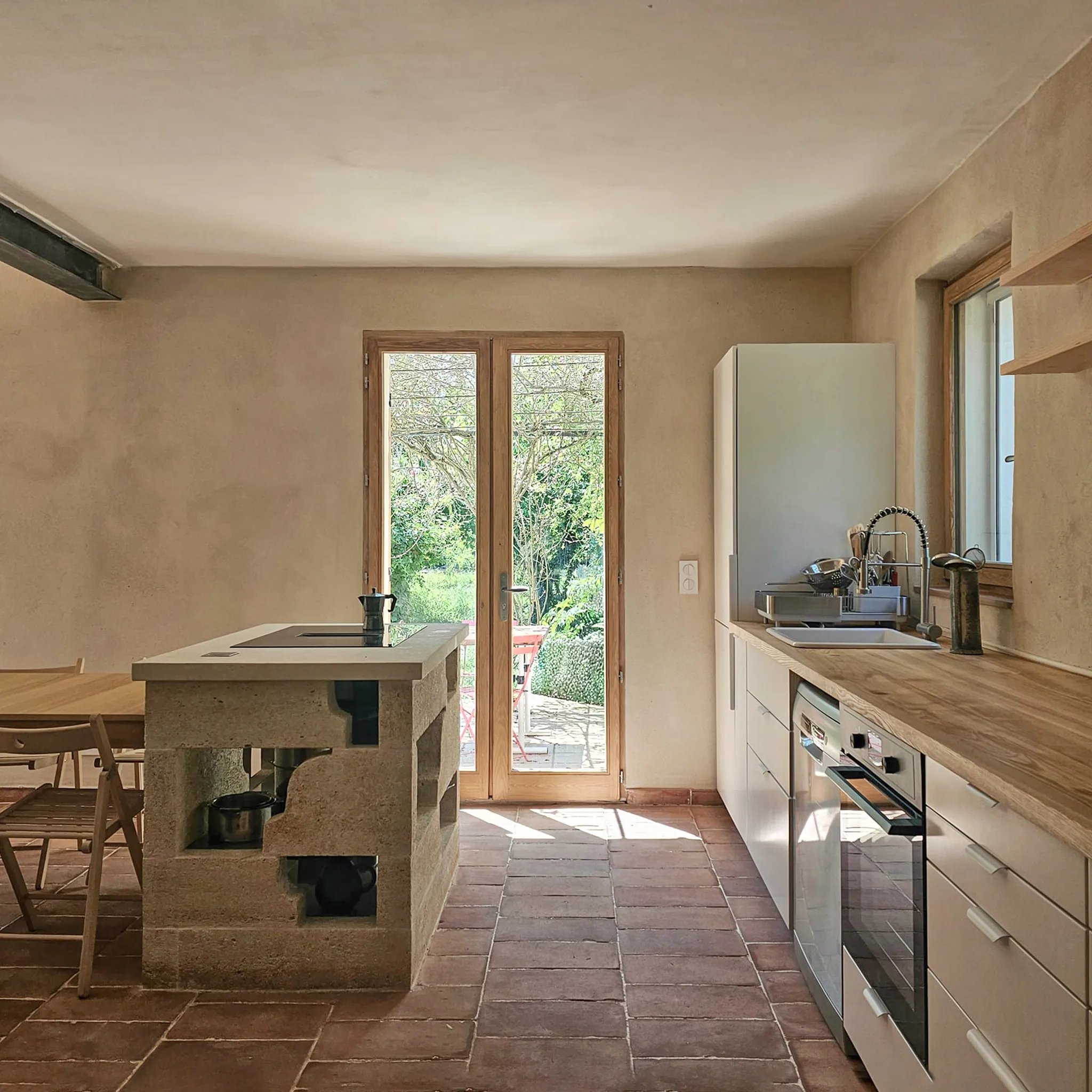 Minimalist kitchen with wooden countertop, stone island, and glass doors opening to garden patio.