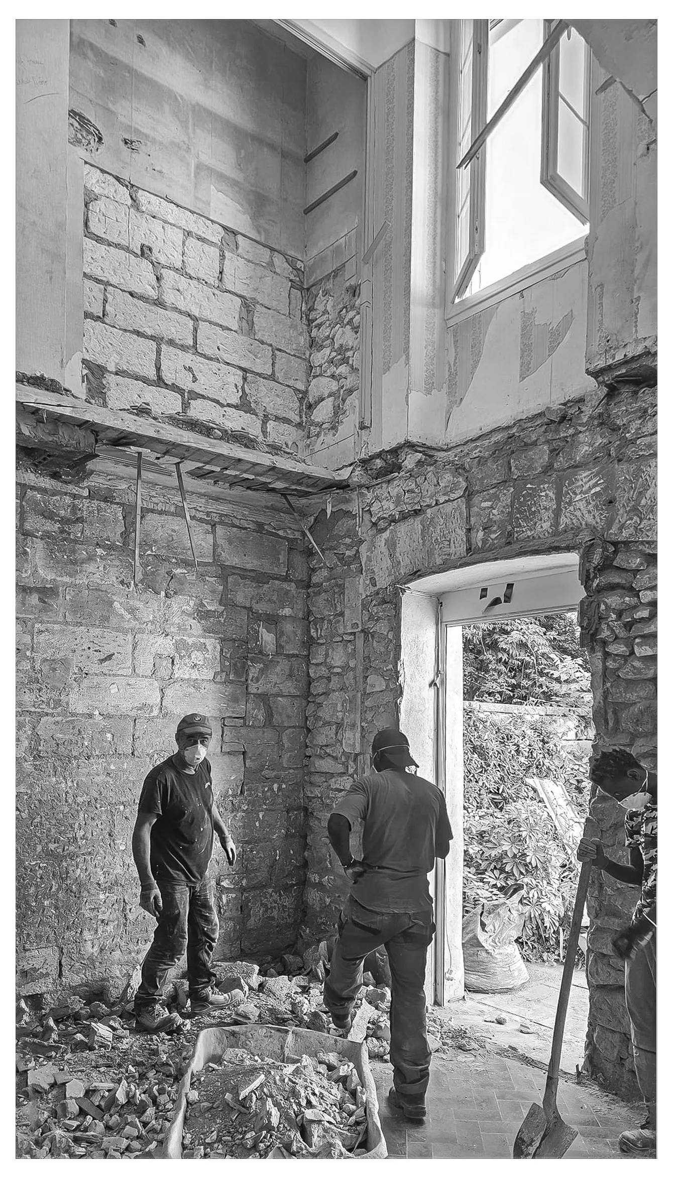 Three workers in masks inside stone building under renovation with rubble and construction tools.