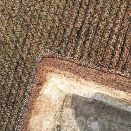 Aerial view of a dirt construction site next to a planted field with shadows of vines.