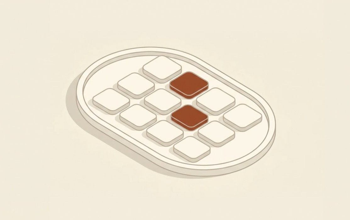 Two brown pill-shaped tablets among ten white tablets on an oval white tray.