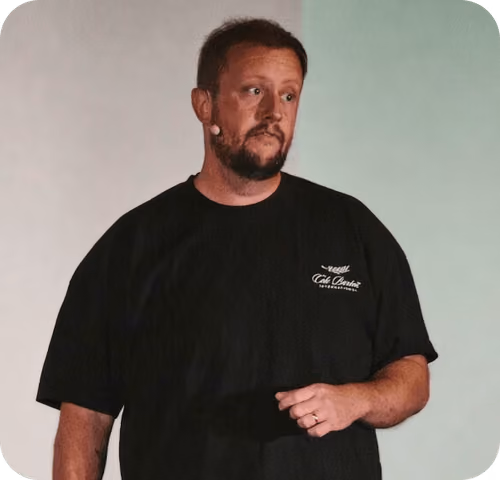 Man with beard and short hair speaking, wearing a black t-shirt and a headset microphone.