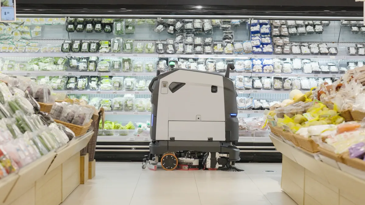PUDU BG1 curățând un culoar de supermarket, printre rafturi cu legume