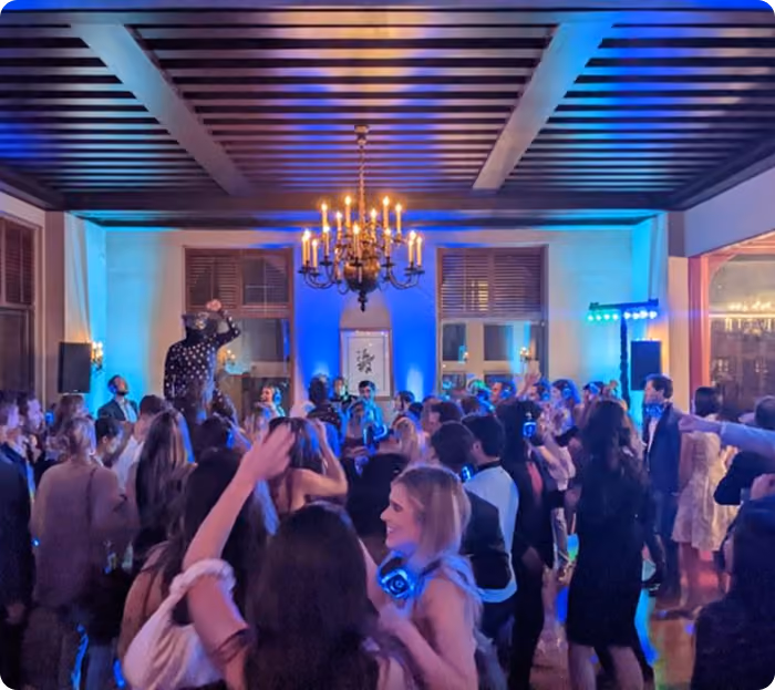 Crowd in silent disco headphones dancing in a ballroom with a chandelier and blue uplighting
