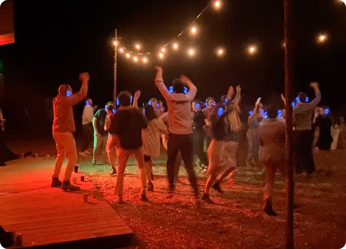 Outdoor silent disco at night with guests dancing on a stage under string lights