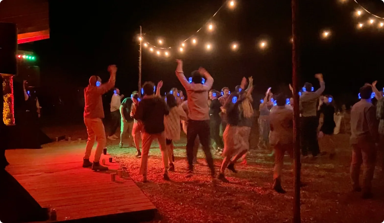 Guests dancing outdoors at night in light-up silent disco headphones under string lights
