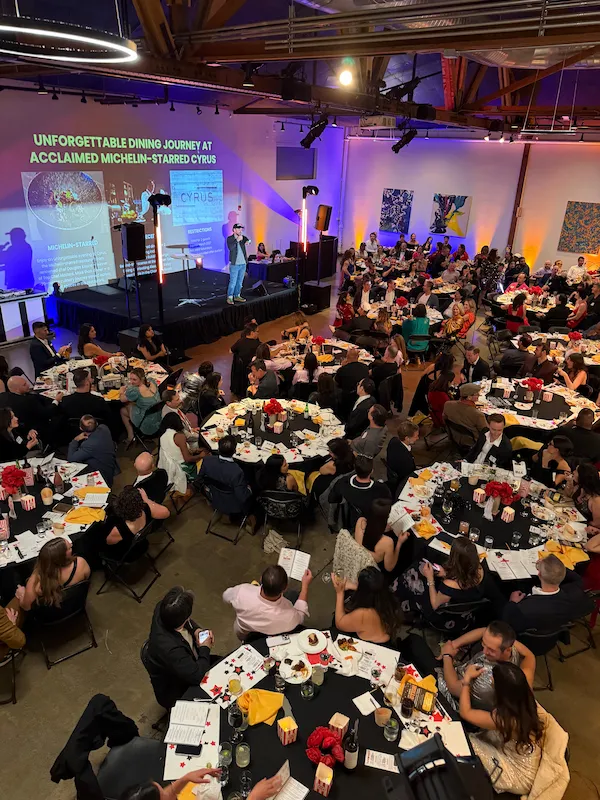 Gala with a stage, projection screens and round banquet tables under purple uplighting