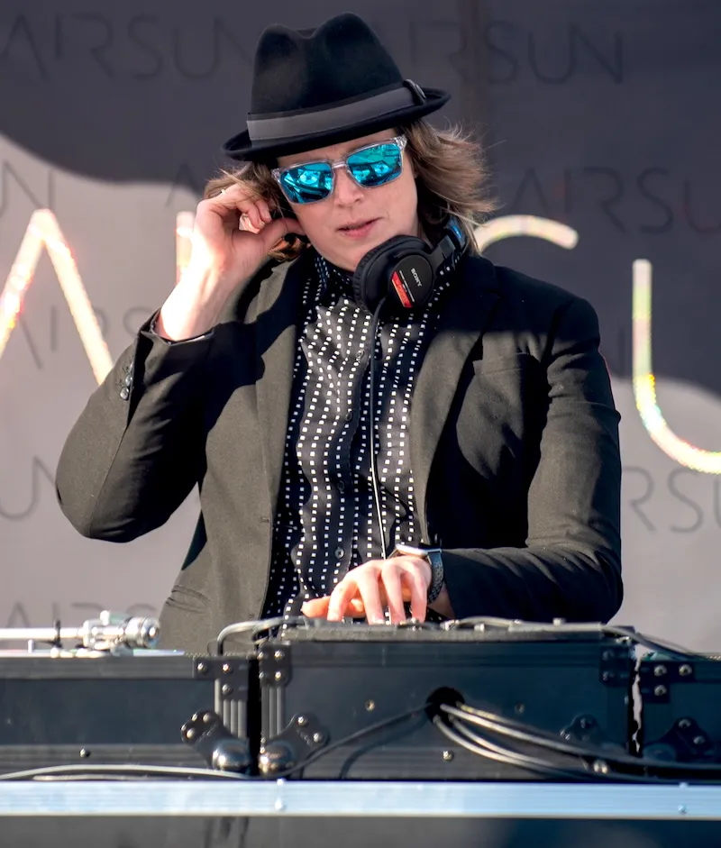 Ersson (DJ Airsun) in a black fedora and sunglasses mixing on DJ decks